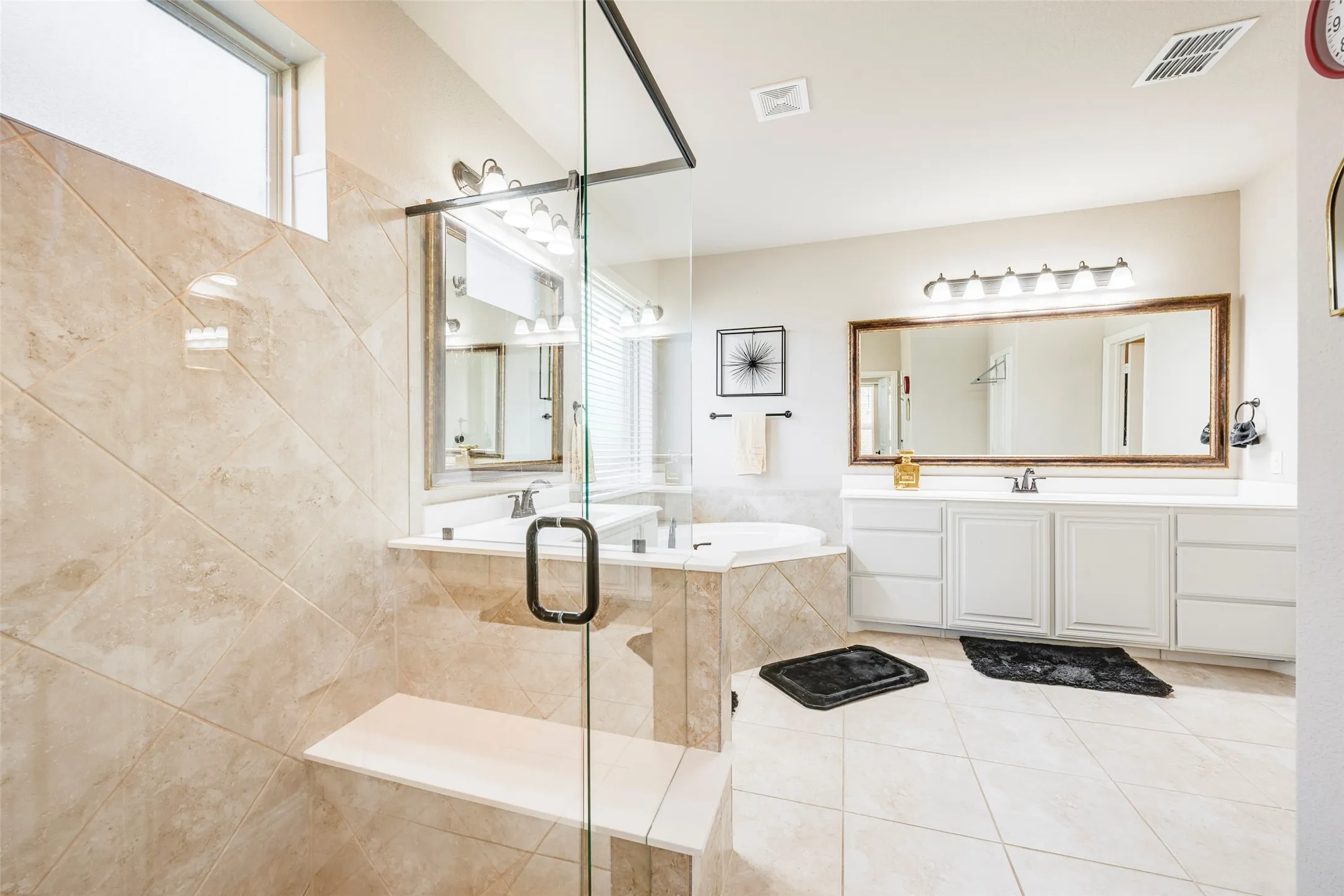 Glass-enclosed shower with a built-in bench, corner soaking tub, dual vanity with undermount sinks, and a large framed mirror