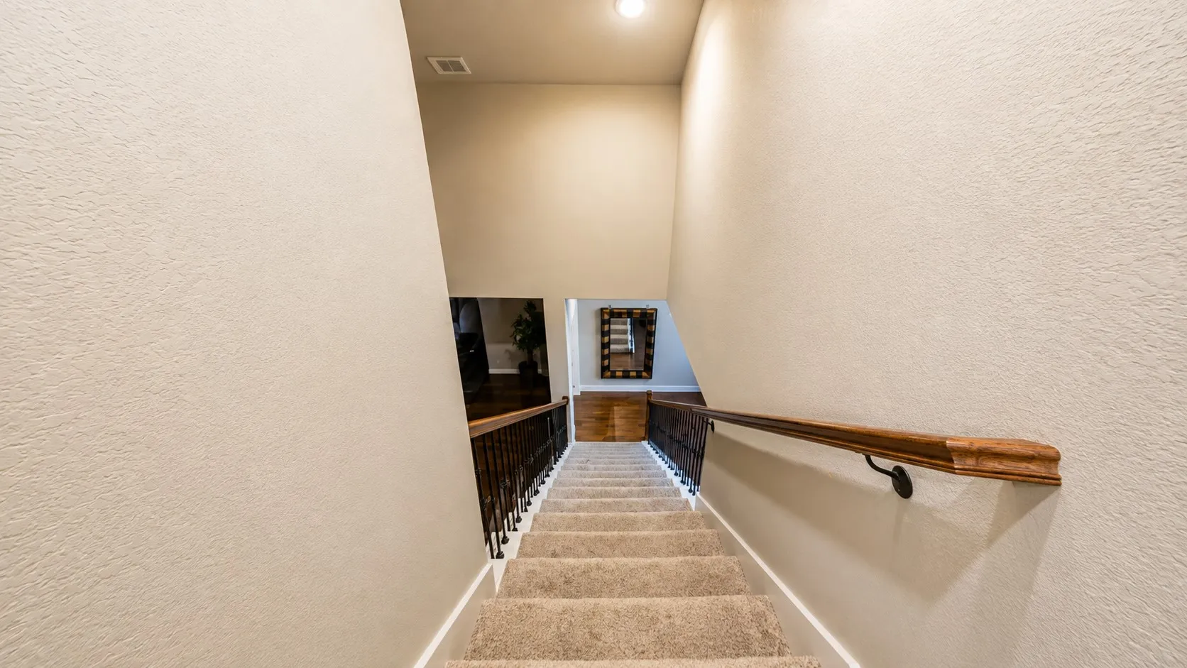 Carpeted staircase with a wood-finish handrail and wrought iron balusters