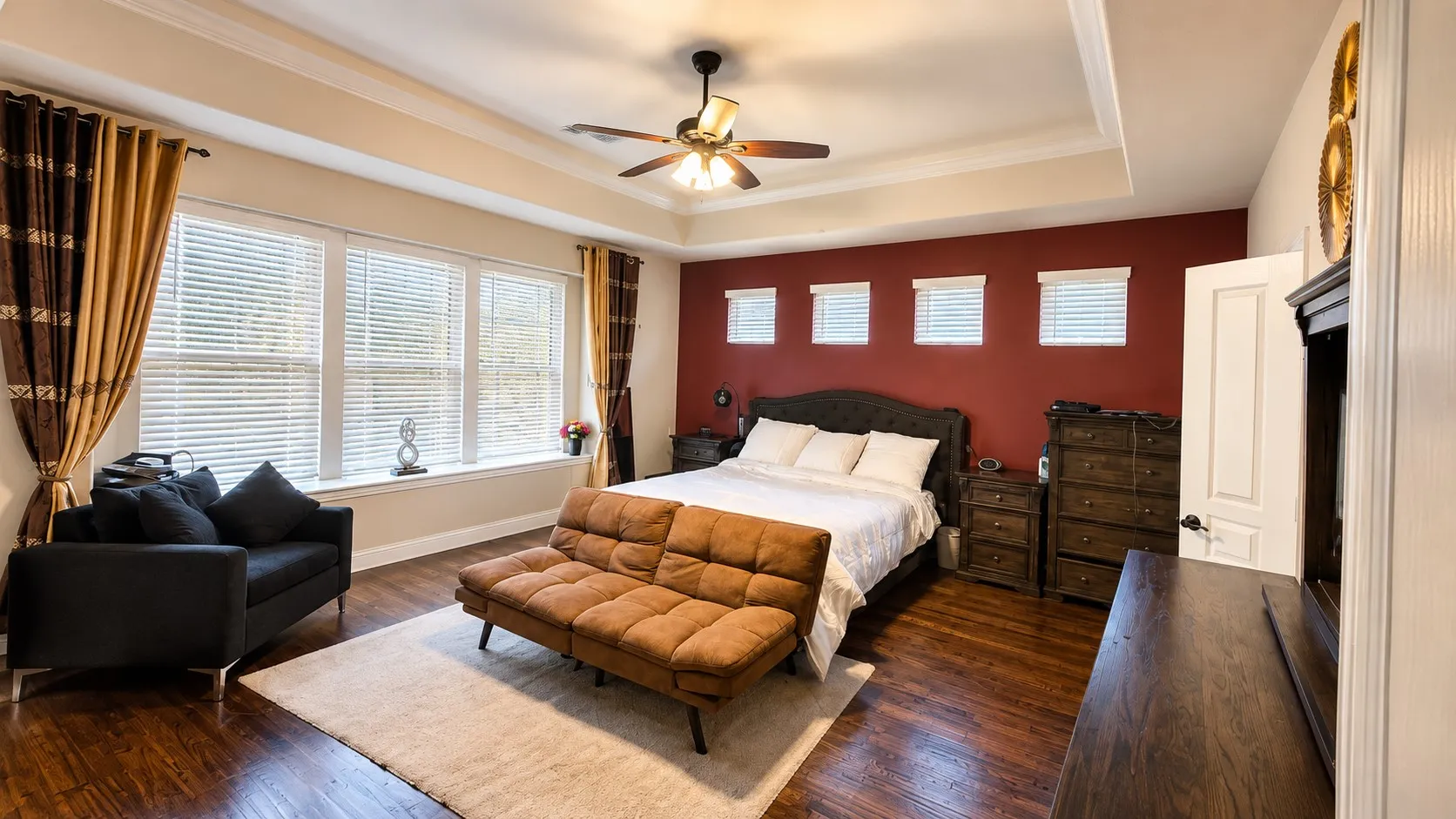 Tray ceiling with crown molding, wood-finish flooring, ceiling fan, and multiple windows with blinds