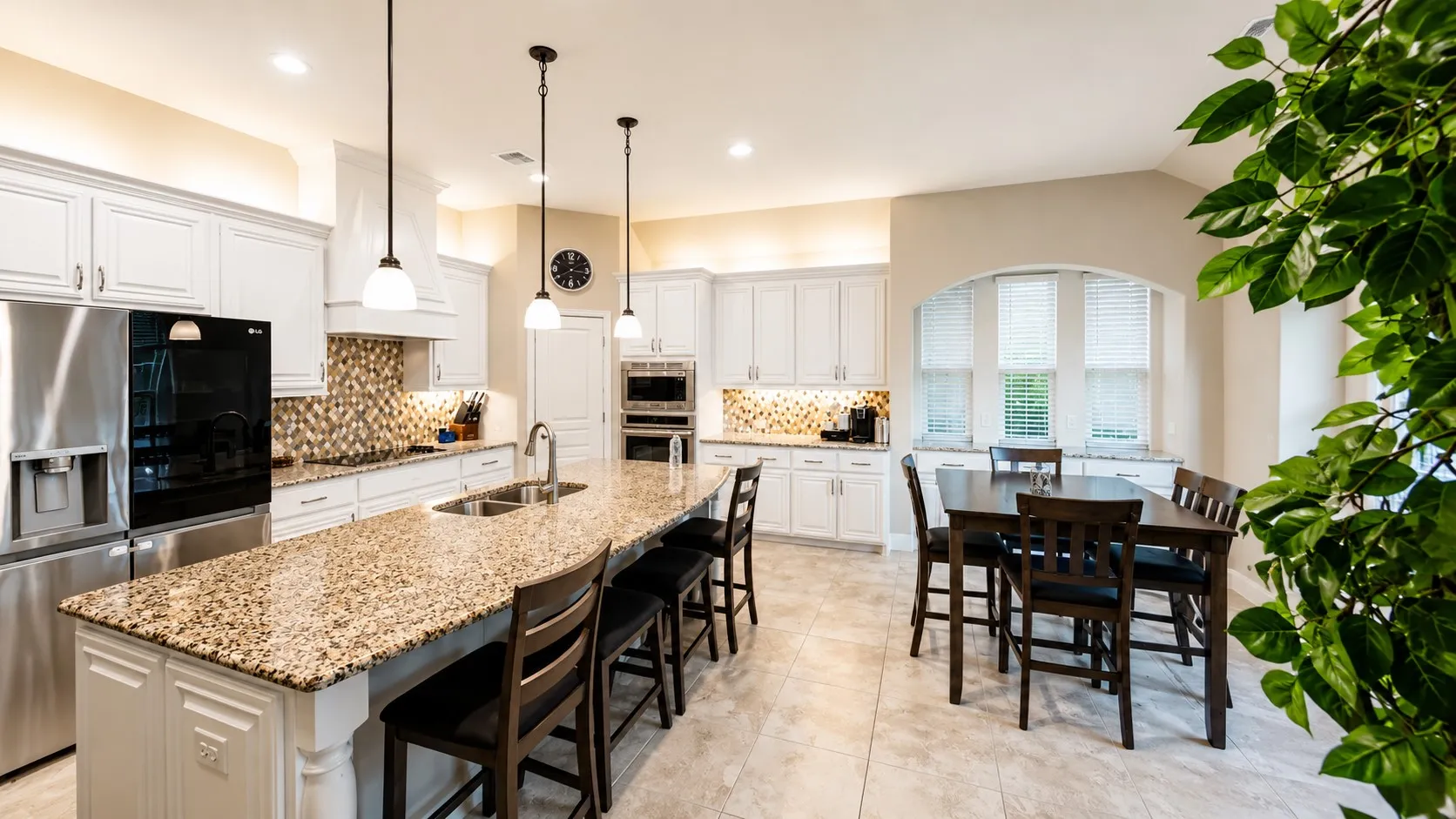 Spacious kitchen featuring an extended island with a dual-basin stainless steel sink, under-cabinet lighting, a built-in oven, and a tiled backsplash