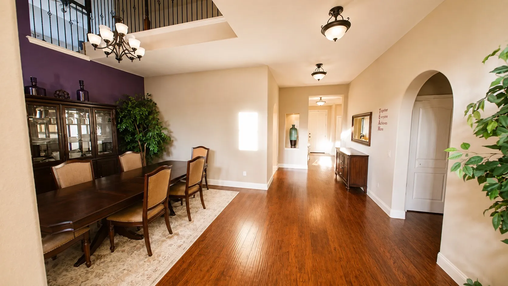 Elegant foyer showcasing rich wood-finish flooring, a curved archway entry, and a two-story ceiling with natural light from upper windows