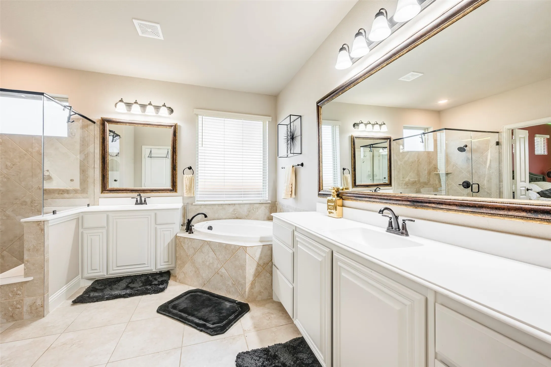 Dual vanities with white cabinetry, a large built-in soaking tub, a separate glass-enclosed shower, and tiled flooring