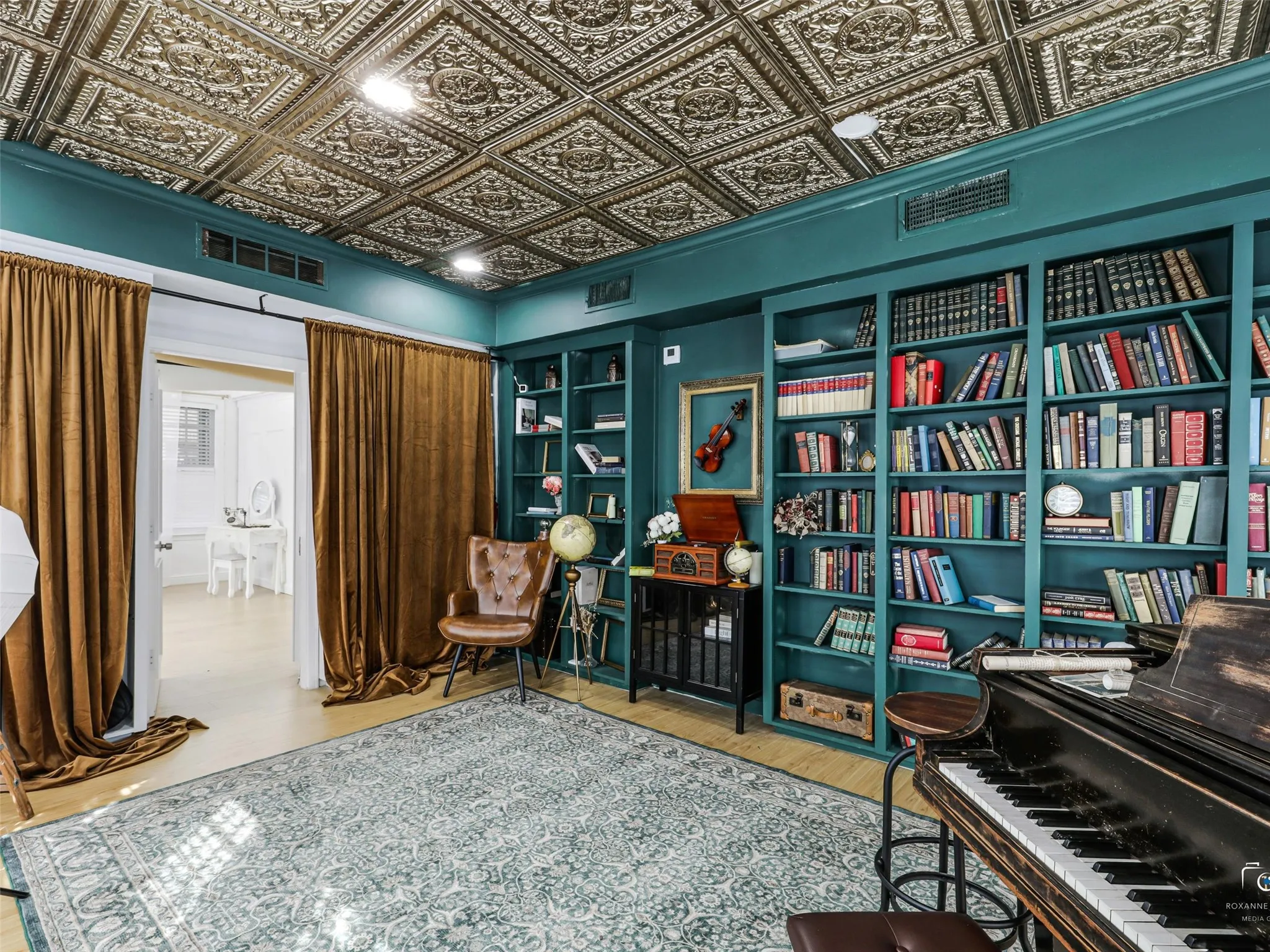 Ornate ceiling with decorative panels, built-in teal shelving, light wood-finish flooring, and a patterned area rug