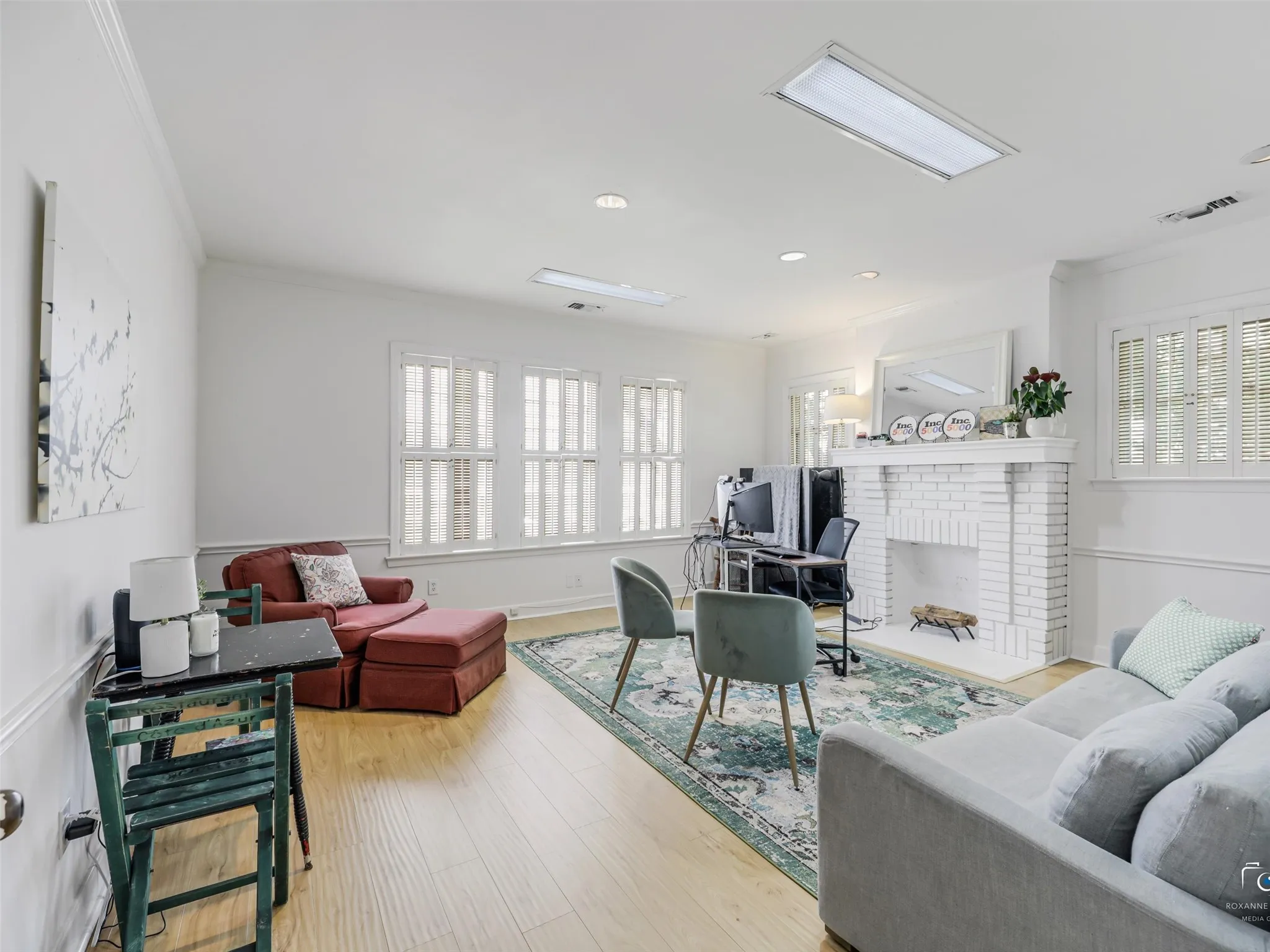 Spacious second floor office featuring wood-finish flooring, white brick fireplace, multiple windows with plantation shutters, recessed lighting