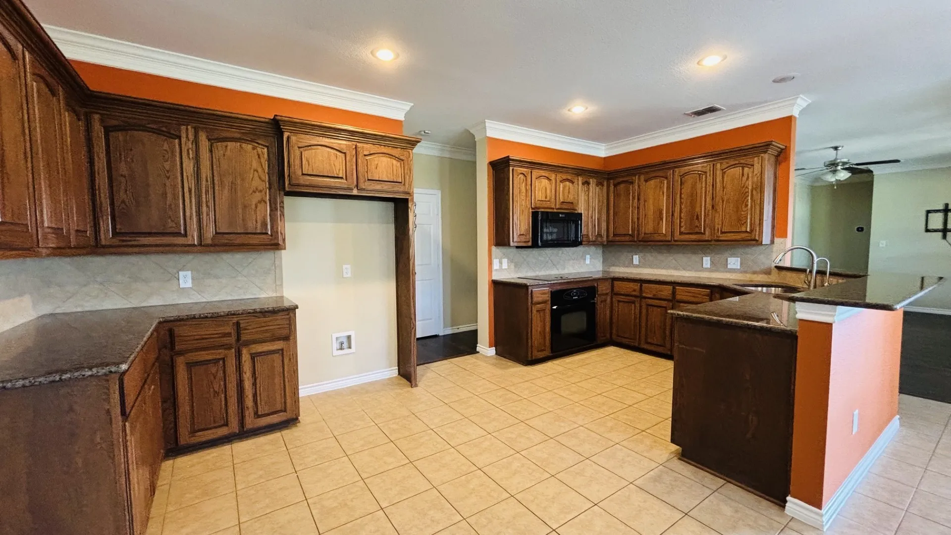 Large kitchen with plenty of storage space, granite countertops, and black appliances.