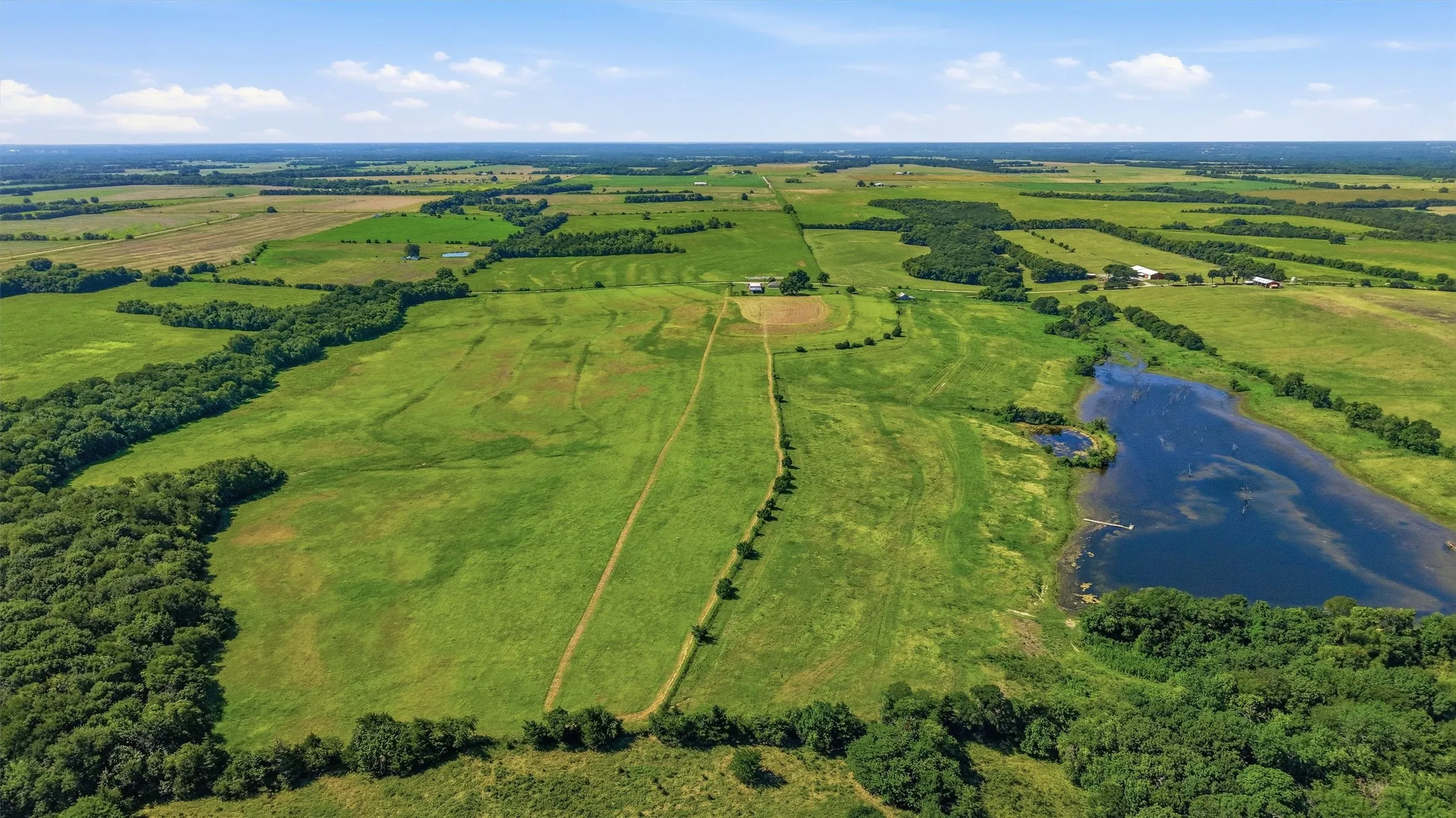 Expansive rural landscape featuring a large body of water, extensive green fields, and clusters of mature trees