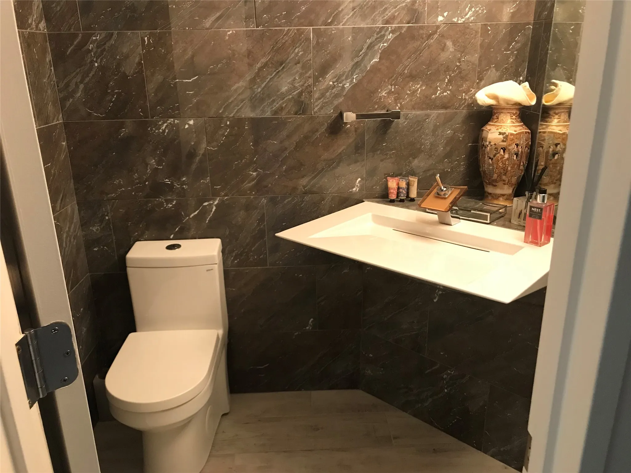 Full-height dark stone-look wall tiling, contemporary white wall-mounted basin, sleek toilet, and a wall-mounted faucet