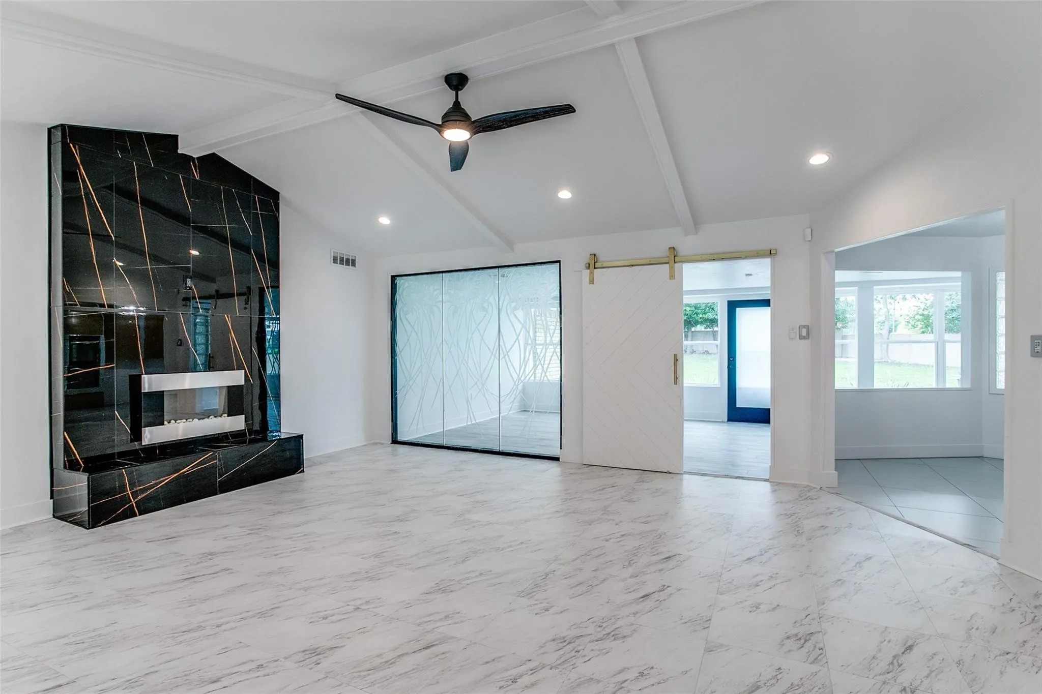 Spacious living area featuring a vaulted ceiling with exposed beams, a dramatic black fireplace with gold veining and a linear insert, and large-format gray marble-look tile flooring