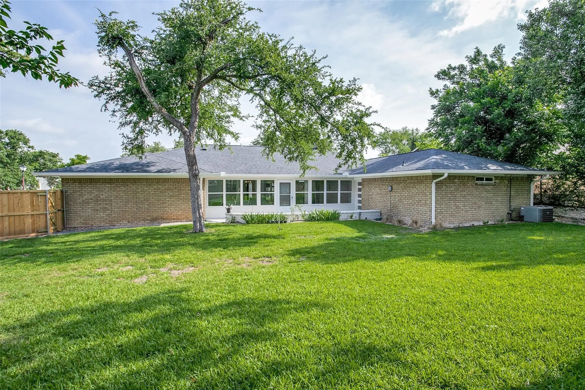 Expansive green lawn with mature tree, brick exterior, and sunroom with multiple windows