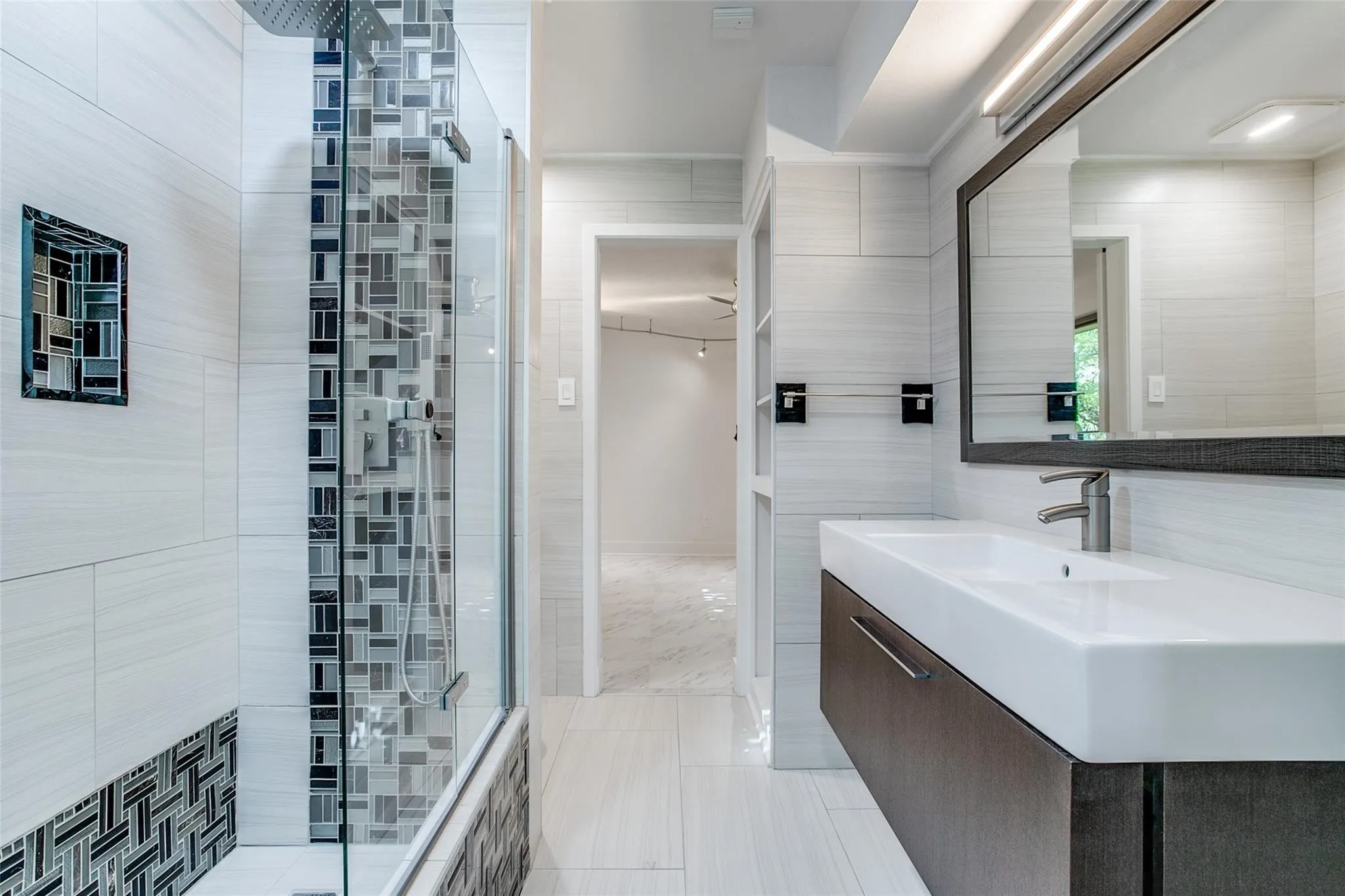 Contemporary bathroom featuring a floating vanity with integrated sink, a framed mirror, and a glass-enclosed shower with mosaic tile accents and a built-in shower niche