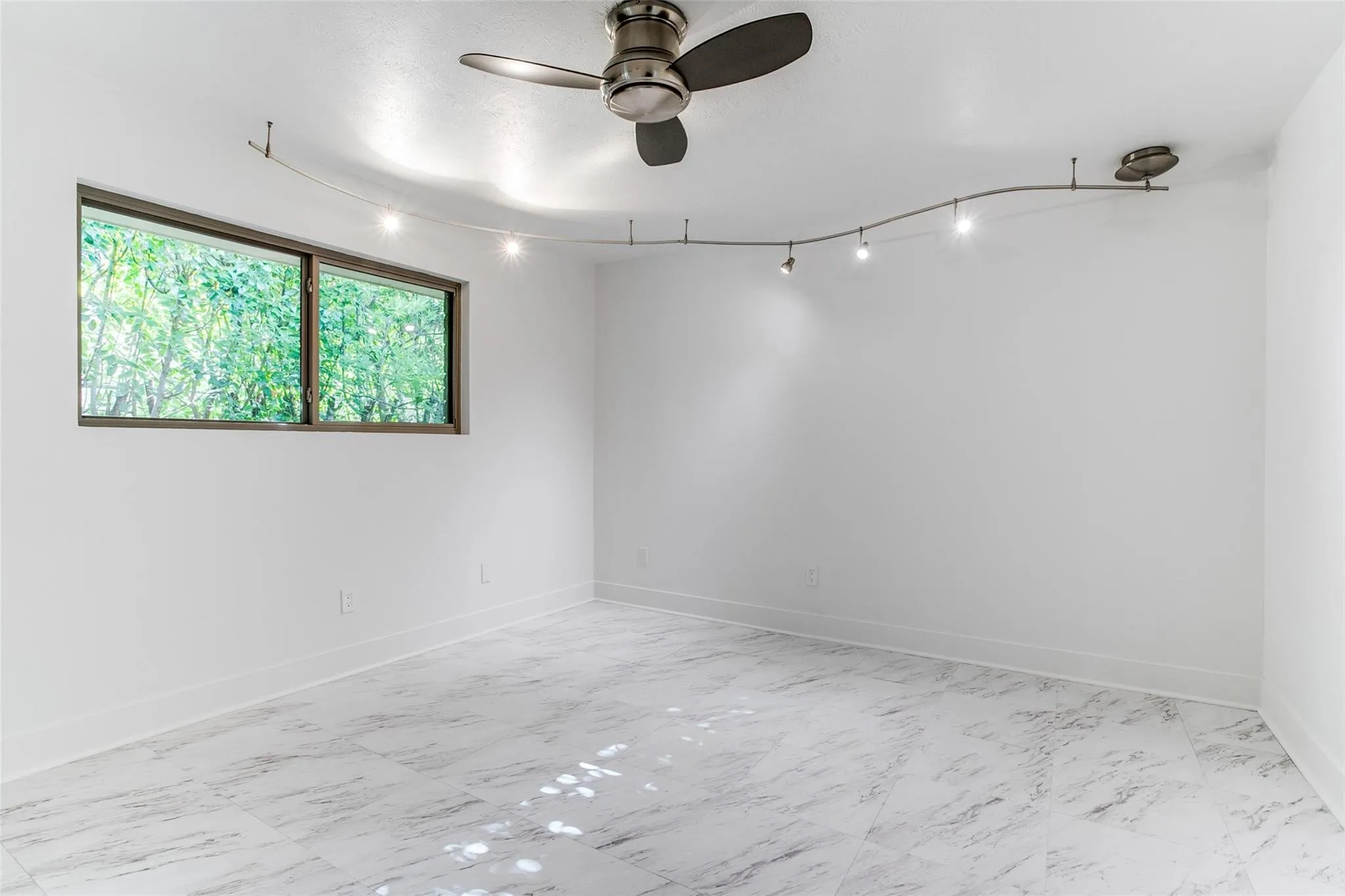Bright room featuring white walls, large window, track lighting, ceiling fan, and light-toned tile flooring