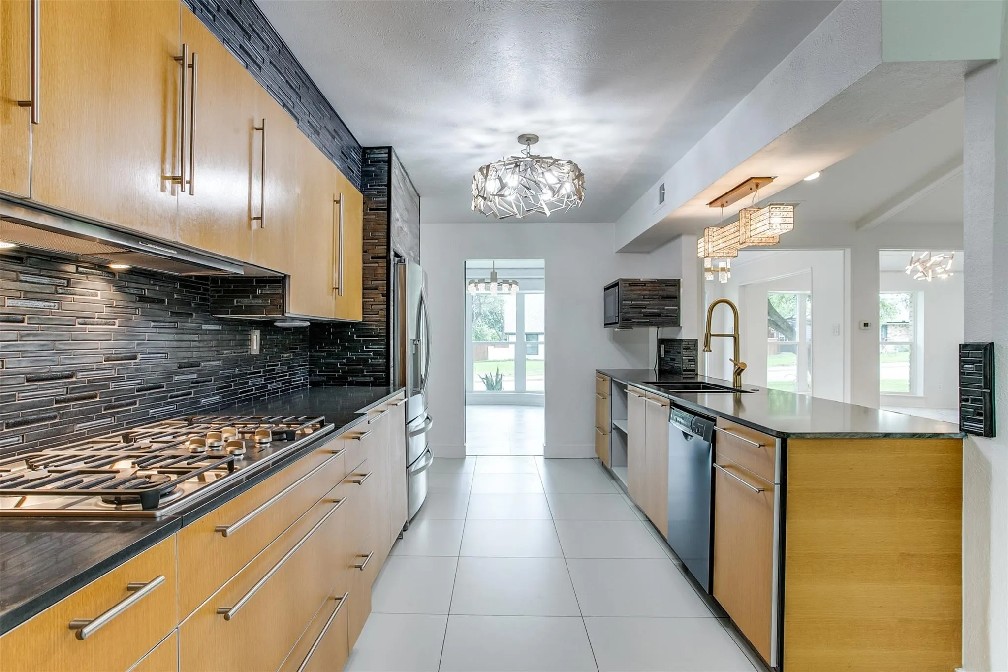 Galley kitchen featuring light wood cabinetry with long bar pulls, dark stone countertops, a stainless steel gas range with a tile backsplash, and white tile flooring
