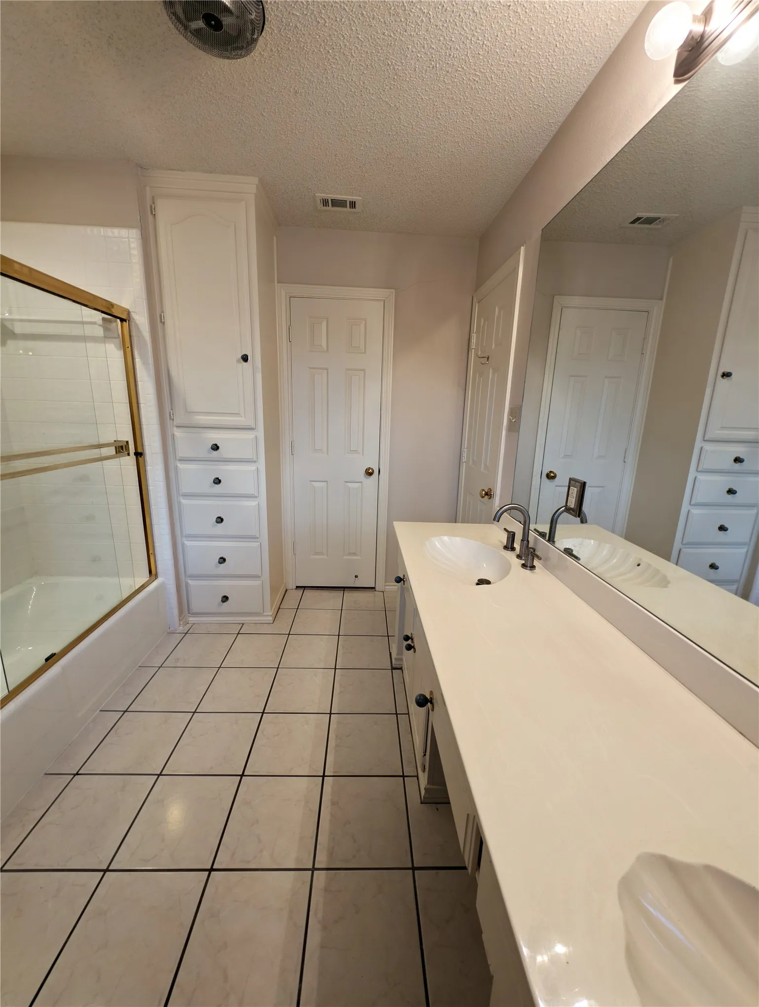 Bathroom featuring a dual vanity with integrated sinks, a lengthy mirrored wall, and built-in white cabinetry
