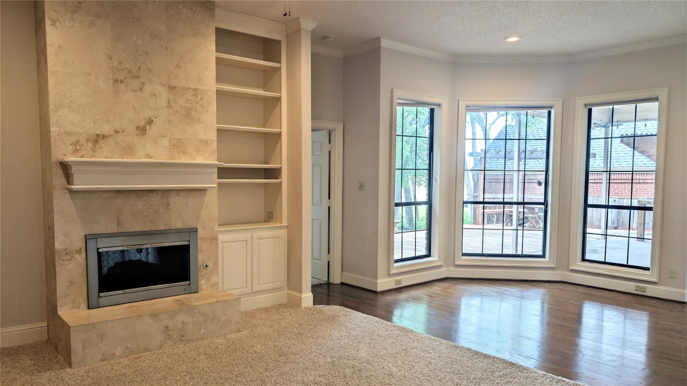 Living area featuring a stone-clad fireplace with mantel, built-in shelving, rich wood-finish flooring, and a bay window with multiple panes