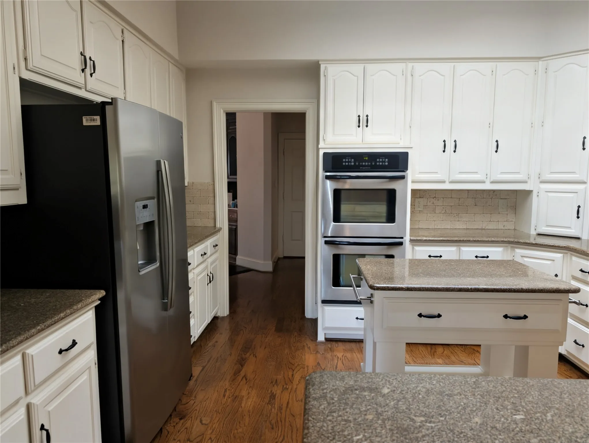 Bright kitchen featuring white cabinetry, stainless steel double ovens, a built-in refrigerator, granite-style countertops, and wood-finish flooring