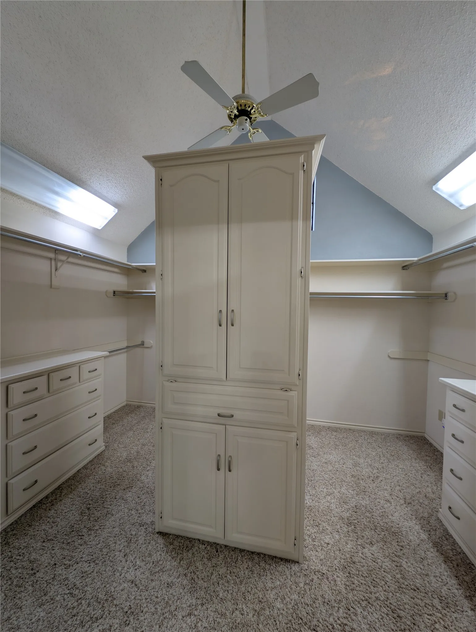 Walk-in closet featuring an angled ceiling, two skylights, and a central built-in storage unit with cabinet doors and drawers