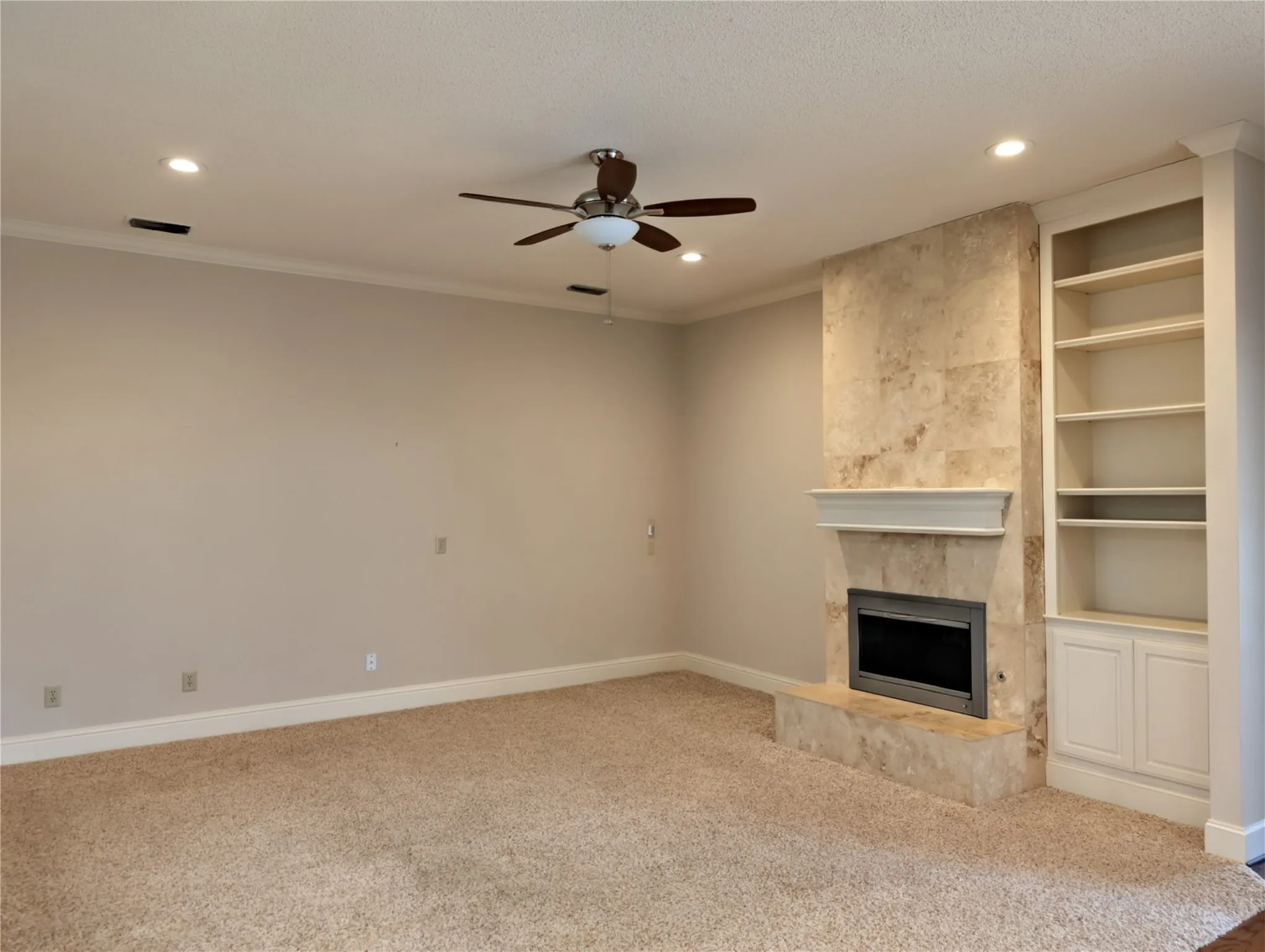 Living area featuring a textured carpet, a stone-clad fireplace with a mantel, built-in shelving with lower cabinetry, recessed lighting, and a ceiling fan