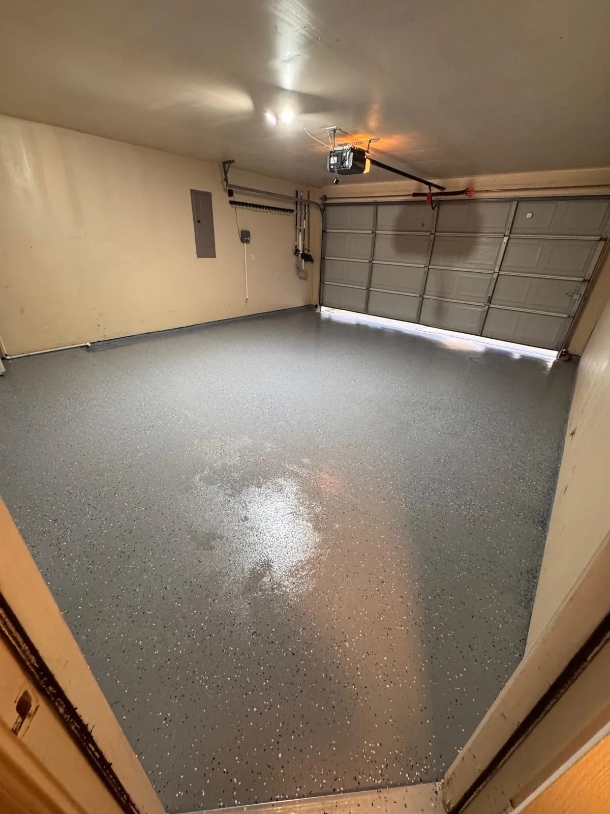 Spacious garage featuring a durable speckled epoxy floor finish, an automatic overhead garage door opener, and a wall-mounted electrical panel