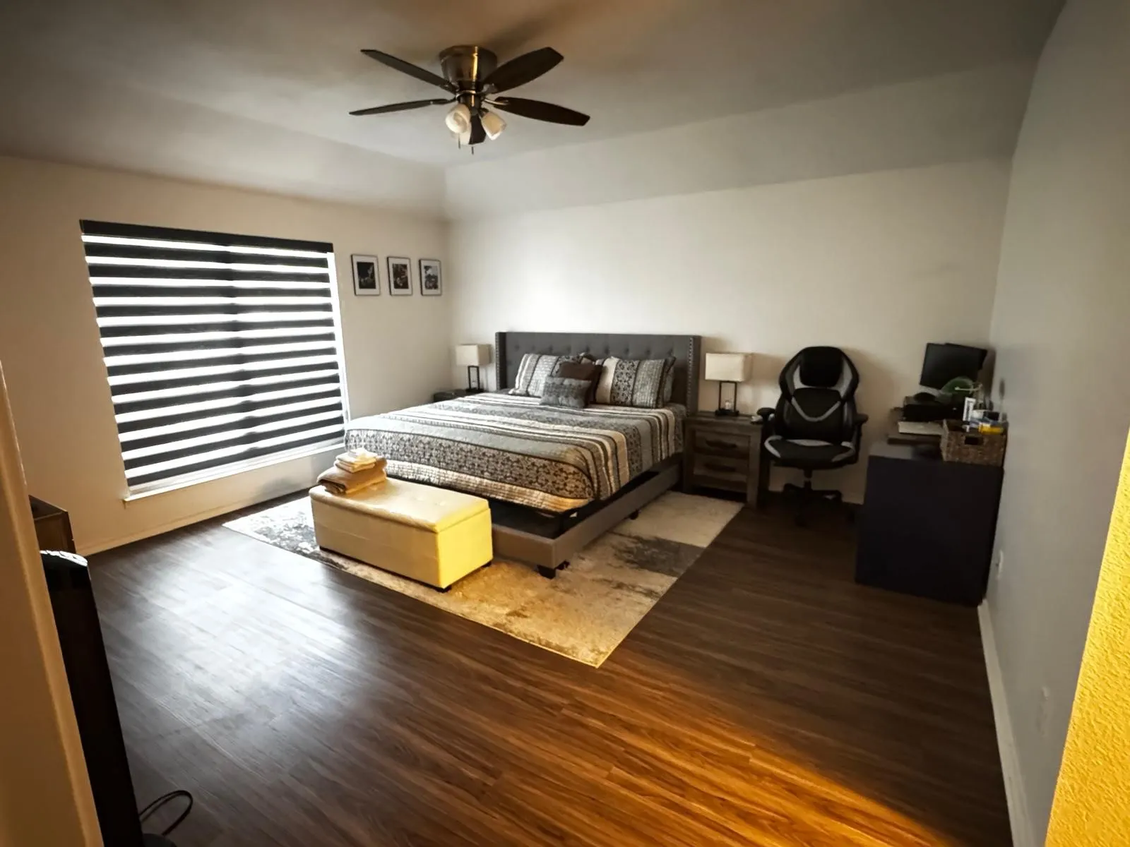 Spacious room featuring wood-finish flooring, a contemporary ceiling fan with integrated lighting, and a window with horizontal banded blinds