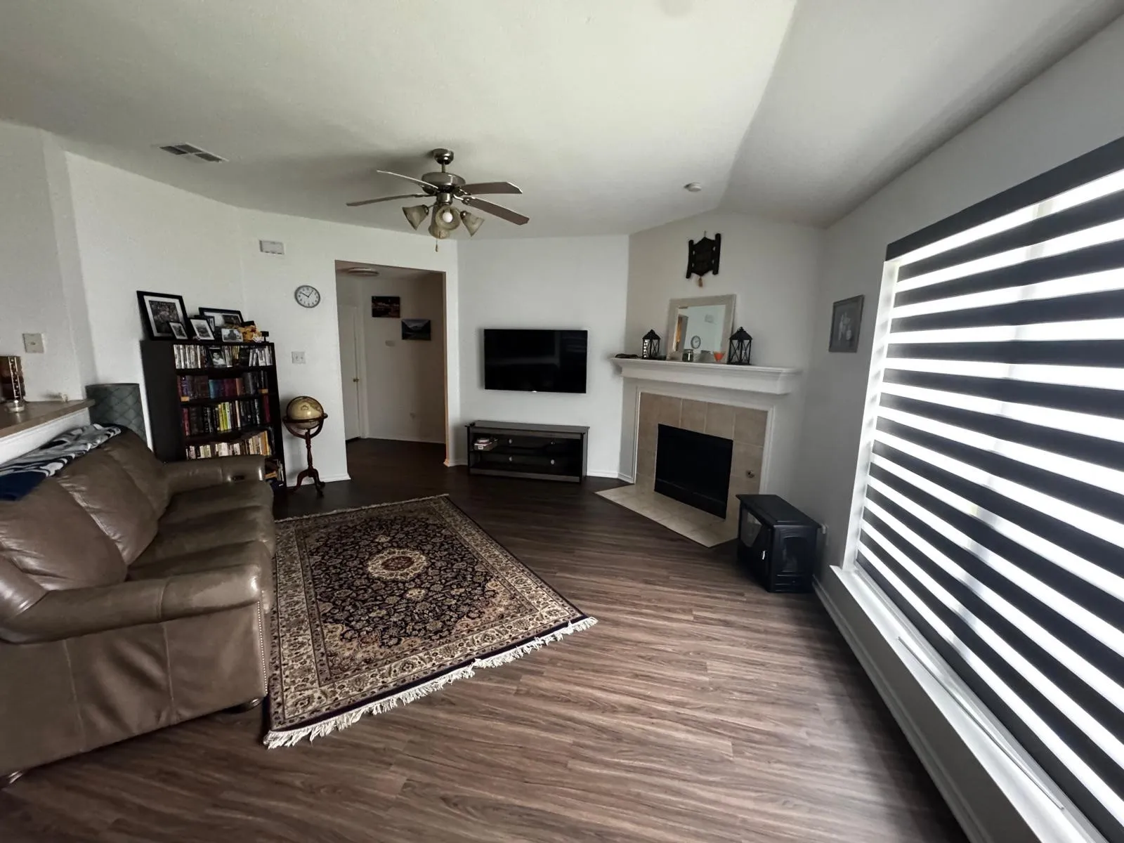 Living area featuring wood-finish flooring, a ceiling fan with integrated lighting, and a fireplace with a tiled surround and mantel