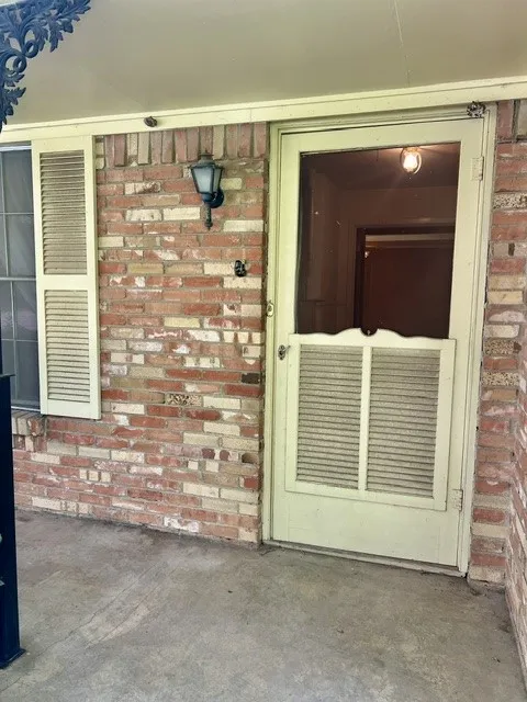 Brick exterior with a covered entryway, showcasing a wall-mounted light fixture and a louvered storm door