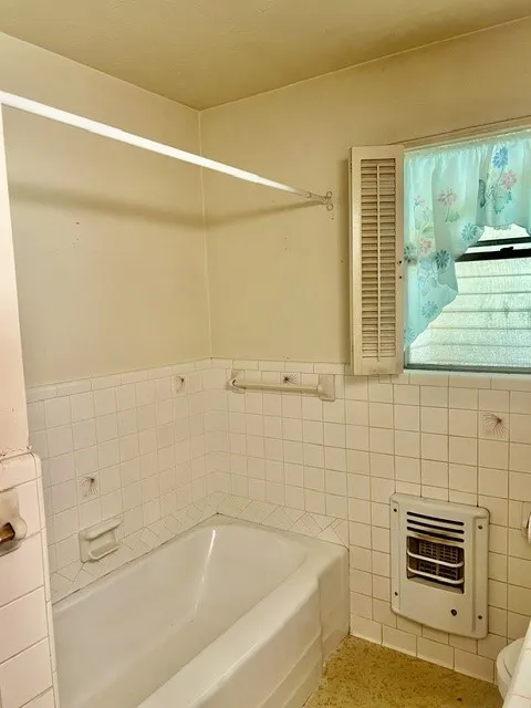 White tile shower surround with a built-in bathtub and a window with louvered shutters
