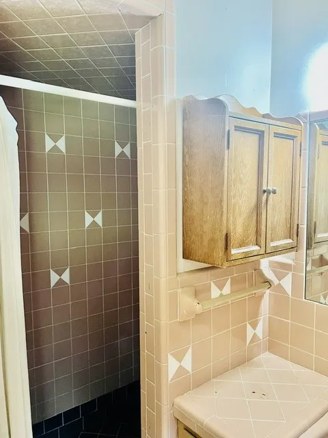 Bathroom featuring a built-in wooden medicine cabinet, a tiled countertop, and a shower area with contrasting tile patterns