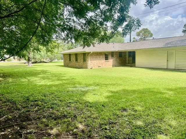 Expansive green lawn surrounds the property, featuring a brick exterior with multiple windows