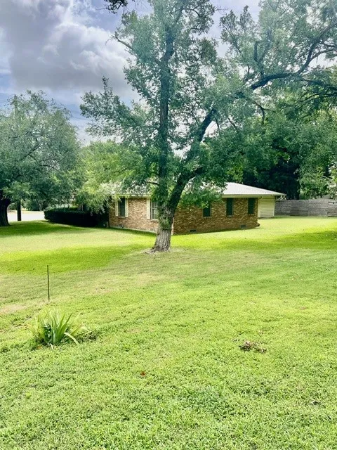 Expansive lawn area featuring mature trees and a brick-clad residence with a white roof