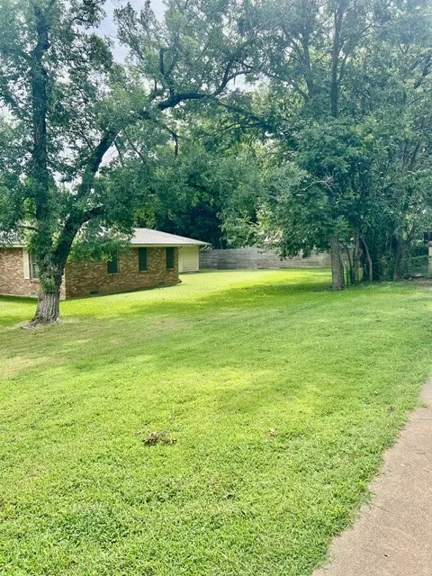 Expansive lawn with mature trees, brick exterior, and a concrete pathway
