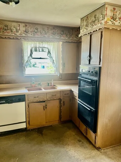 Kitchen featuring wood-finish cabinetry, a double basin sink, built-in double oven, and a dishwasher