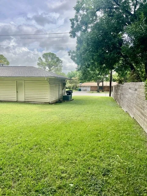 Expansive green lawn area featuring a wooden privacy fence, mature trees, and a detached structure with siding and a dark shingled roof