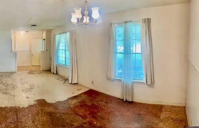 Room featuring two large windows, a decorative chandelier, and exposed subflooring