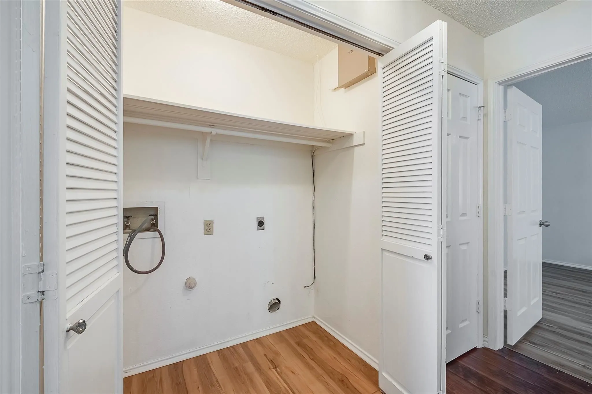 Dedicated laundry closet featuring louvered bi-fold doors, wood-finish flooring, and an integrated storage shelf