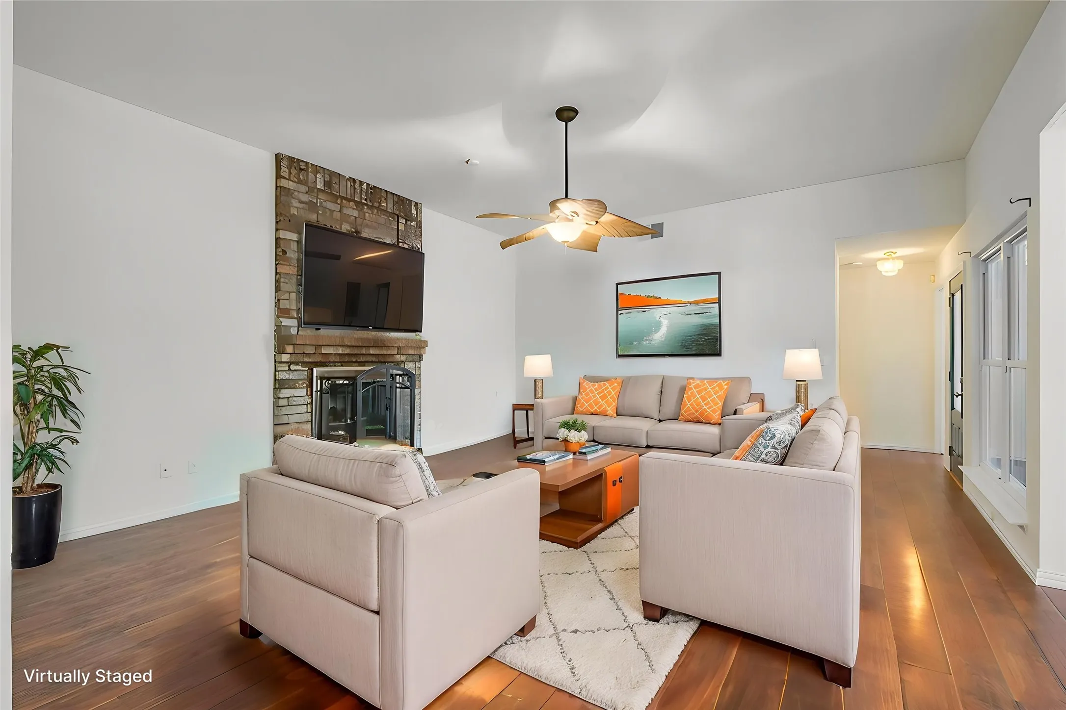 Living area featuring a brick fireplace with a metal fire screen, wood-finish flooring, a ceiling fan with integrated lighting, white walls, and a vaulted ceiling