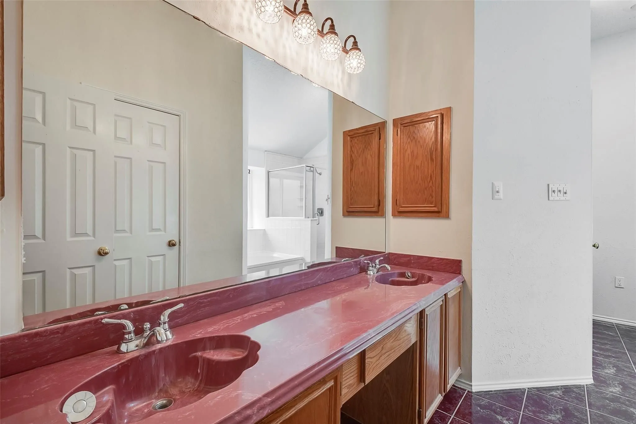 Dual vanity with red countertop and integrated sinks, wood cabinetry, and overhead decorative lighting