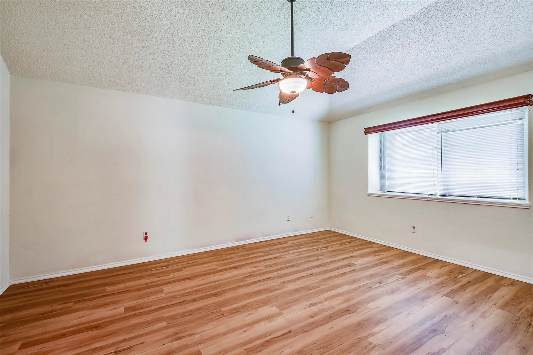 Spacious room featuring wood-finish flooring, white walls, and a textured ceiling