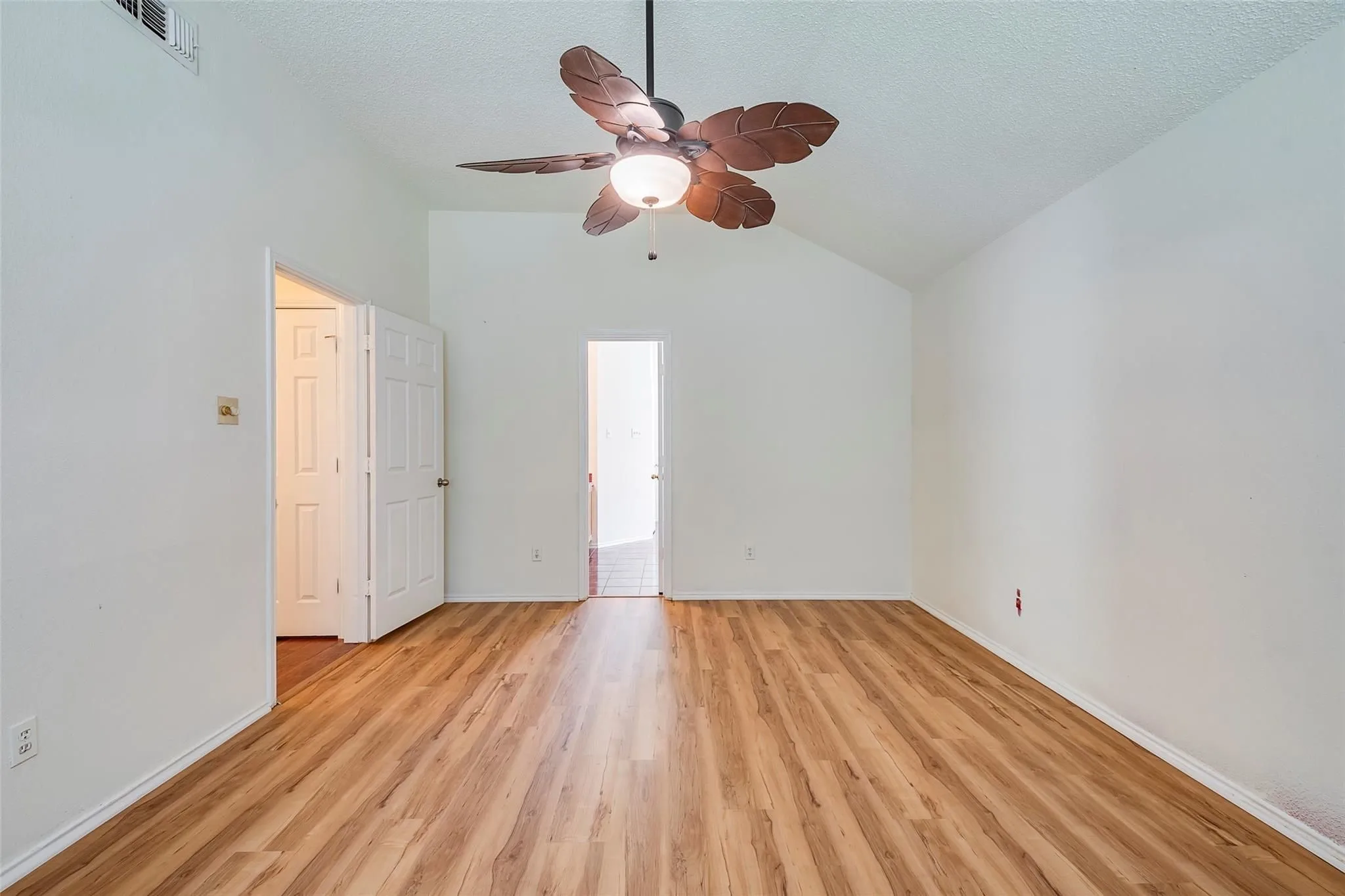 Room featuring high vaulted ceilings, wood-finish flooring, a ceiling fan with integrated lighting, and white paneled doors