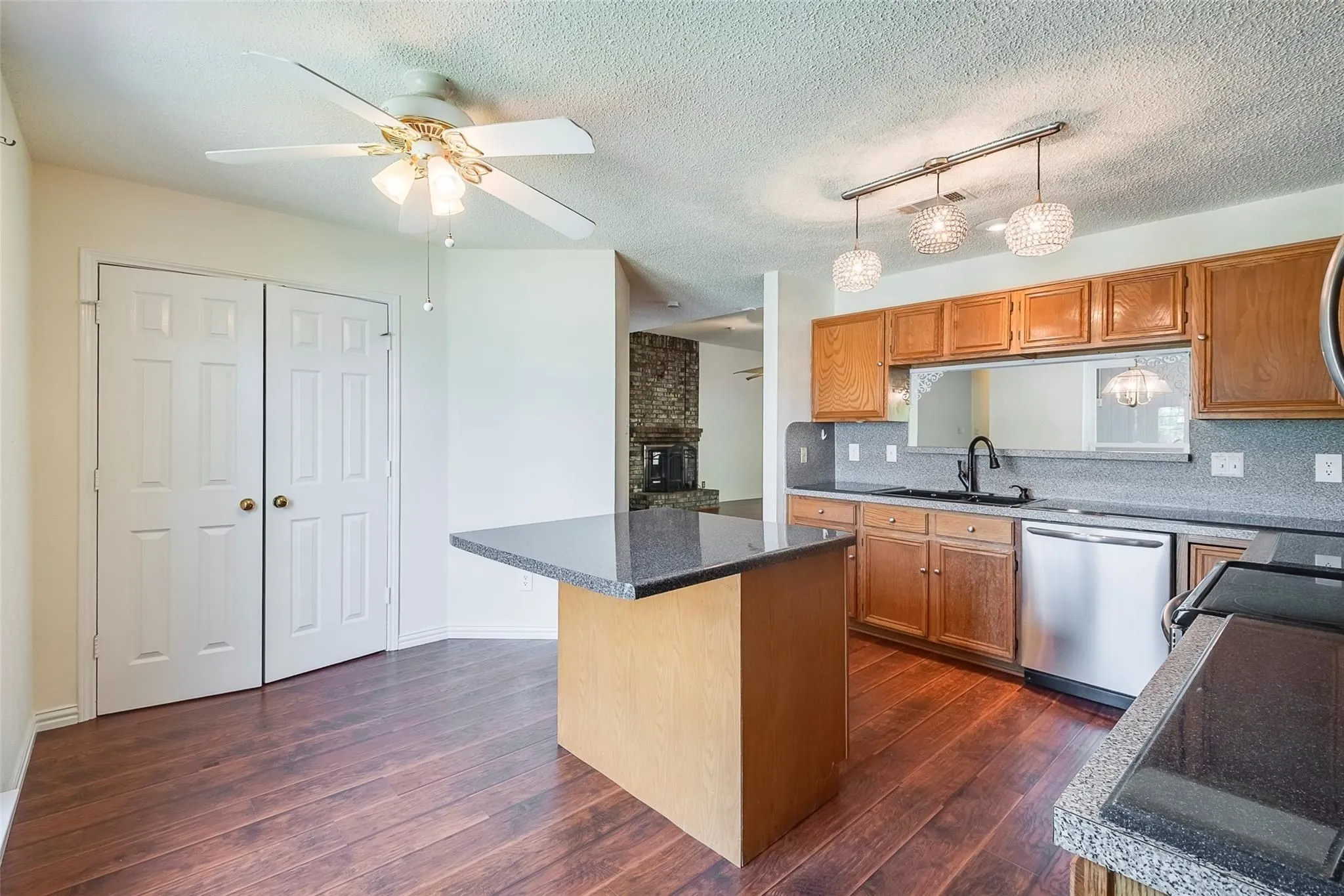 Kitchen featuring wood-finish flooring, a central island with a dark countertop, wood cabinetry, stainless steel appliances, and decorative pendant lighting