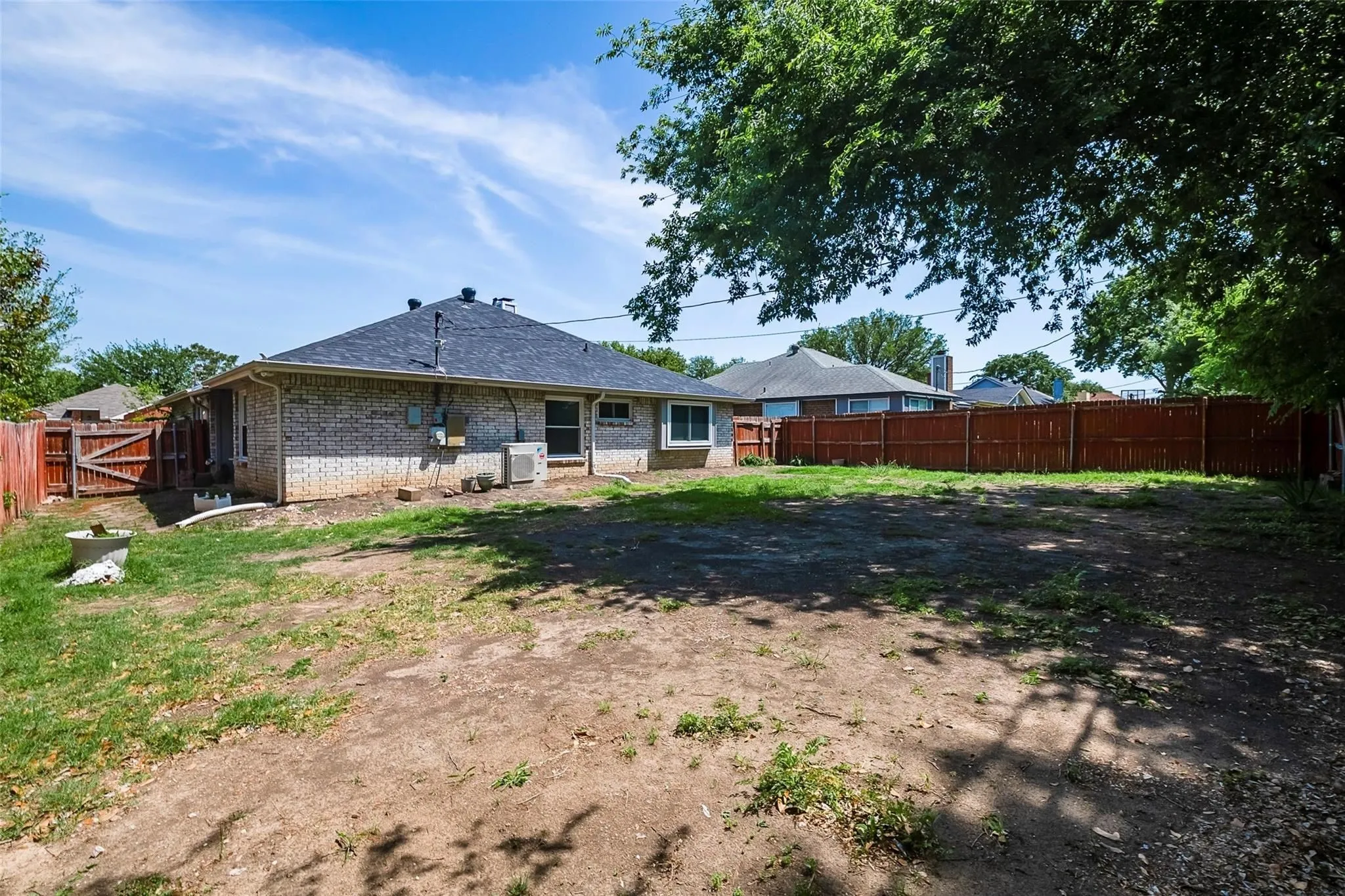 Expansive backyard featuring a full perimeter fence, mature trees, and a brick exterior home with a dark shingle roof