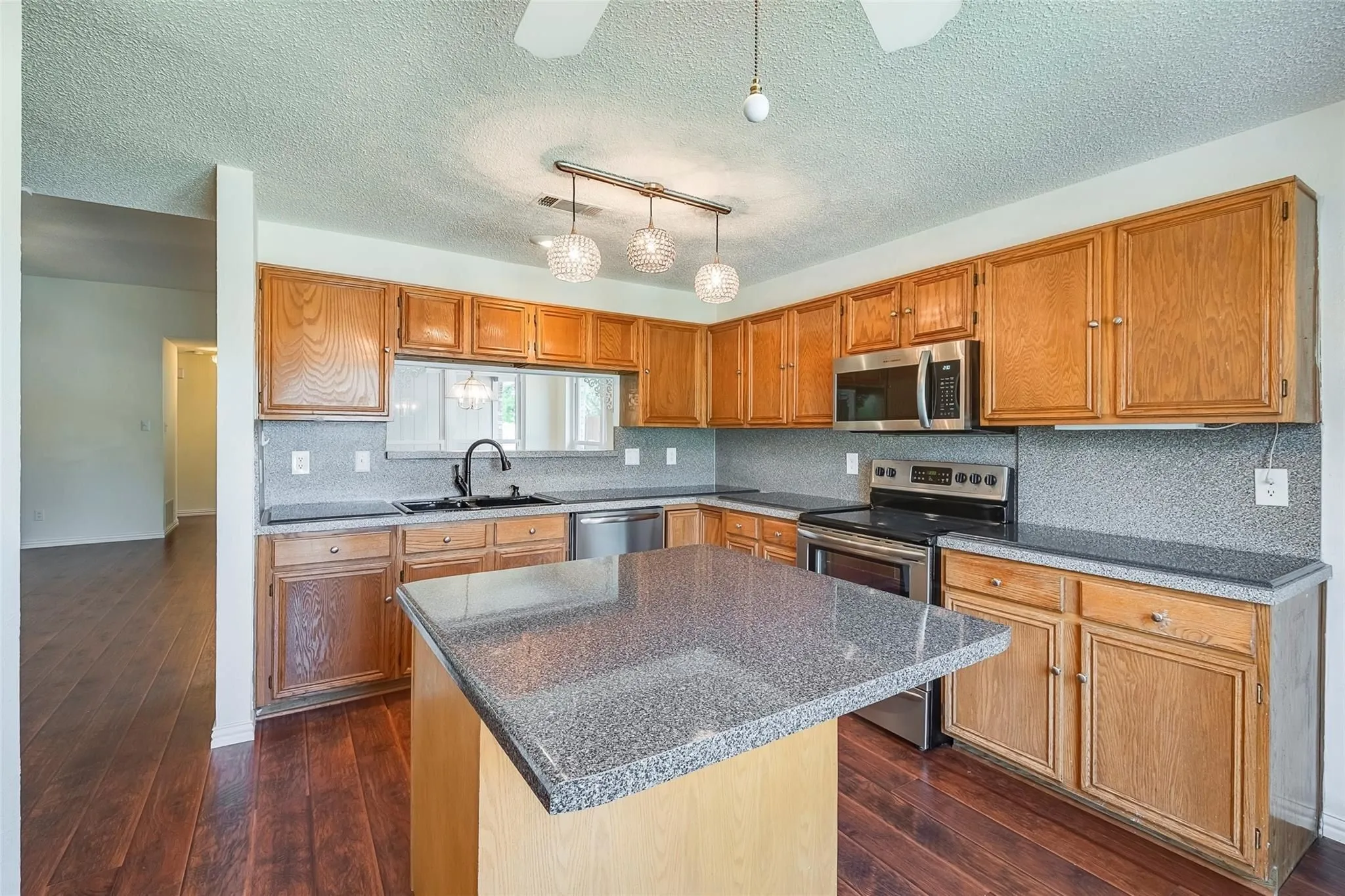 Kitchen featuring wood-finish flooring, an island with a stone-finish countertop, wood cabinetry, stainless steel appliances, and a tile backsplash