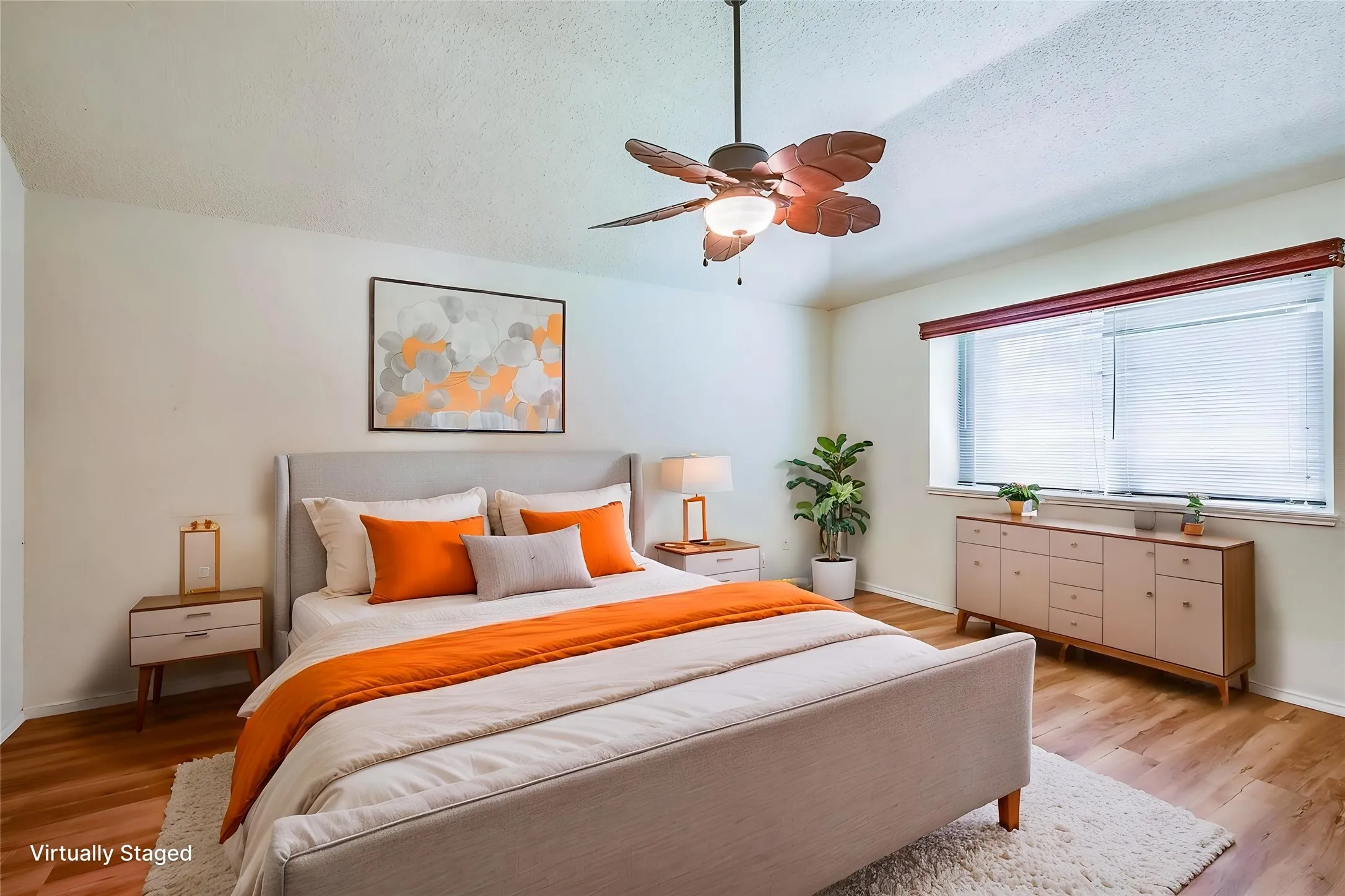 Spacious bedroom featuring warm wood-finish flooring, a large window with blinds, and a ceiling fan with light fixture
