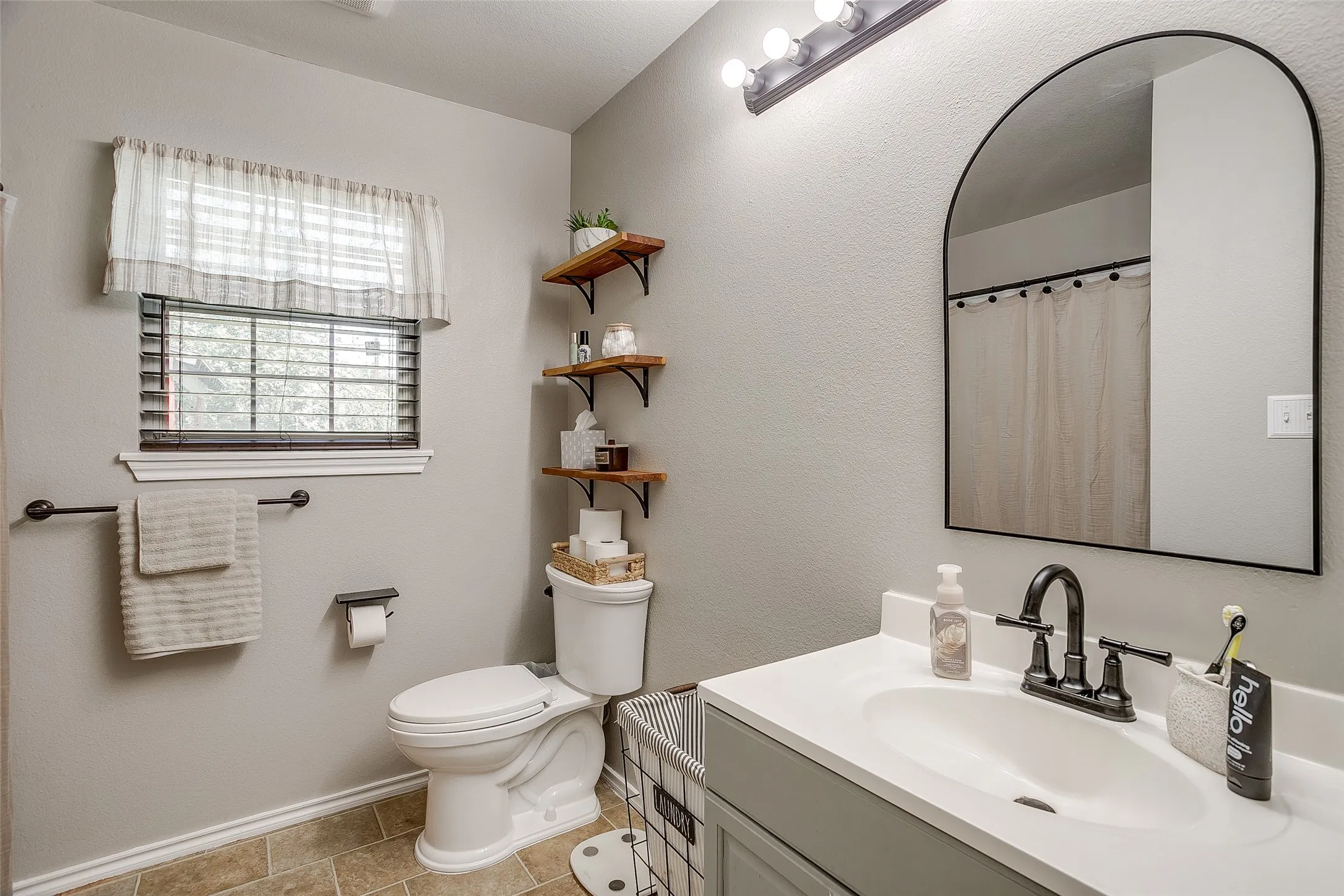Bathroom featuring a white vanity with a single basin sink, matte black faucet, and an arched mirror