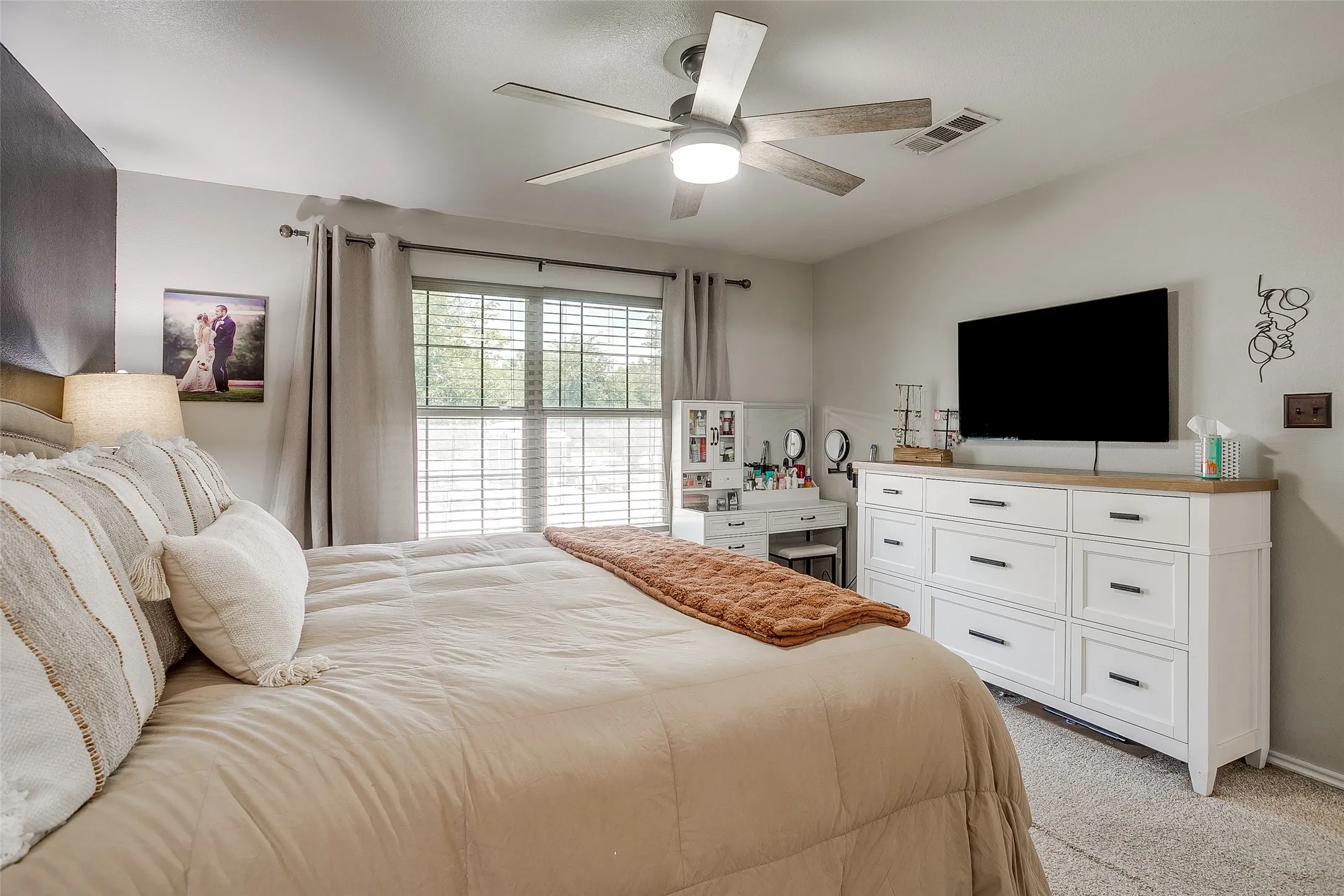 Window with horizontal blinds and drapery panels, featuring a ceiling fan with light fixture, light gray wall paint, and light-toned carpet flooring
