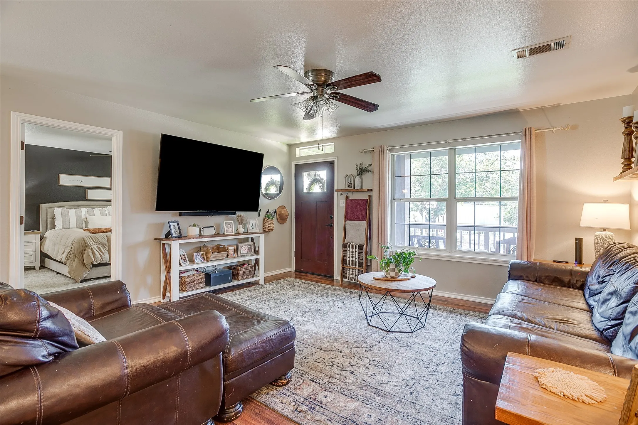 Living room featuring wood-finish flooring, a ceiling fan with light fixture, and a white-trimmed window