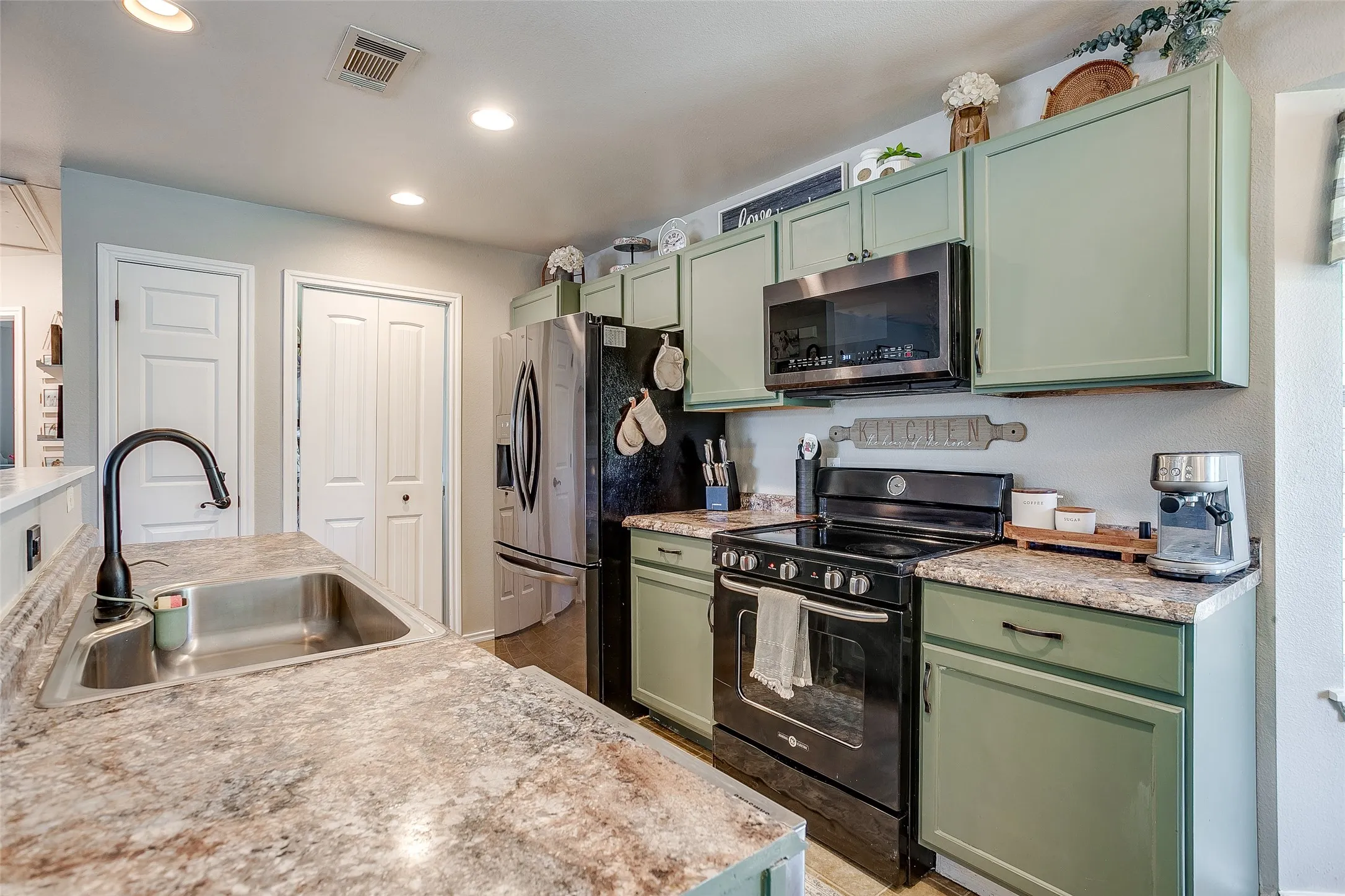 Kitchen featuring sage green cabinetry, stainless steel sink with a gooseneck faucet, black electric range, and an over-the-range microwave