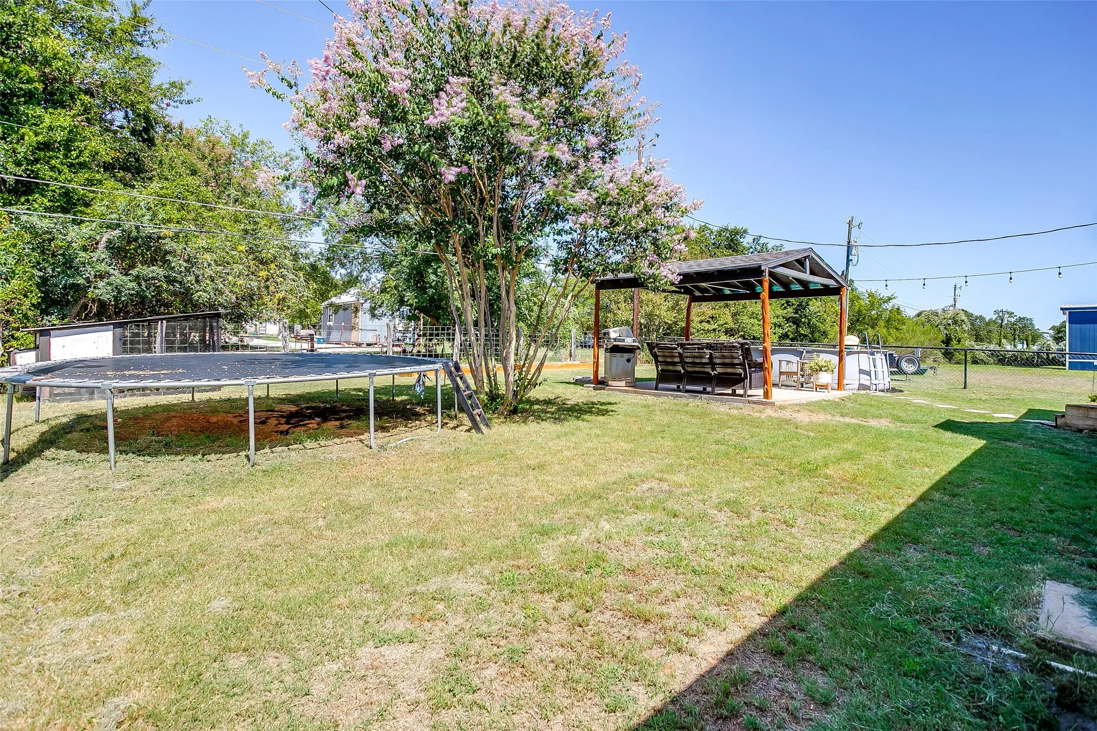 Expansive backyard featuring a mature flowering tree and a covered outdoor entertaining area with a built-in grill station