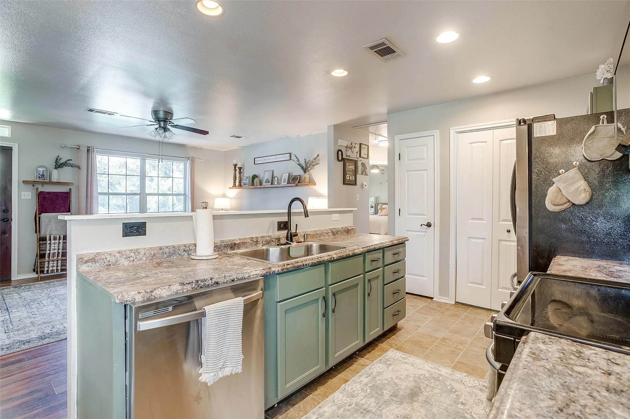 Kitchen featuring a stainless steel sink with a black gooseneck faucet, light green cabinetry, and granite-style countertops