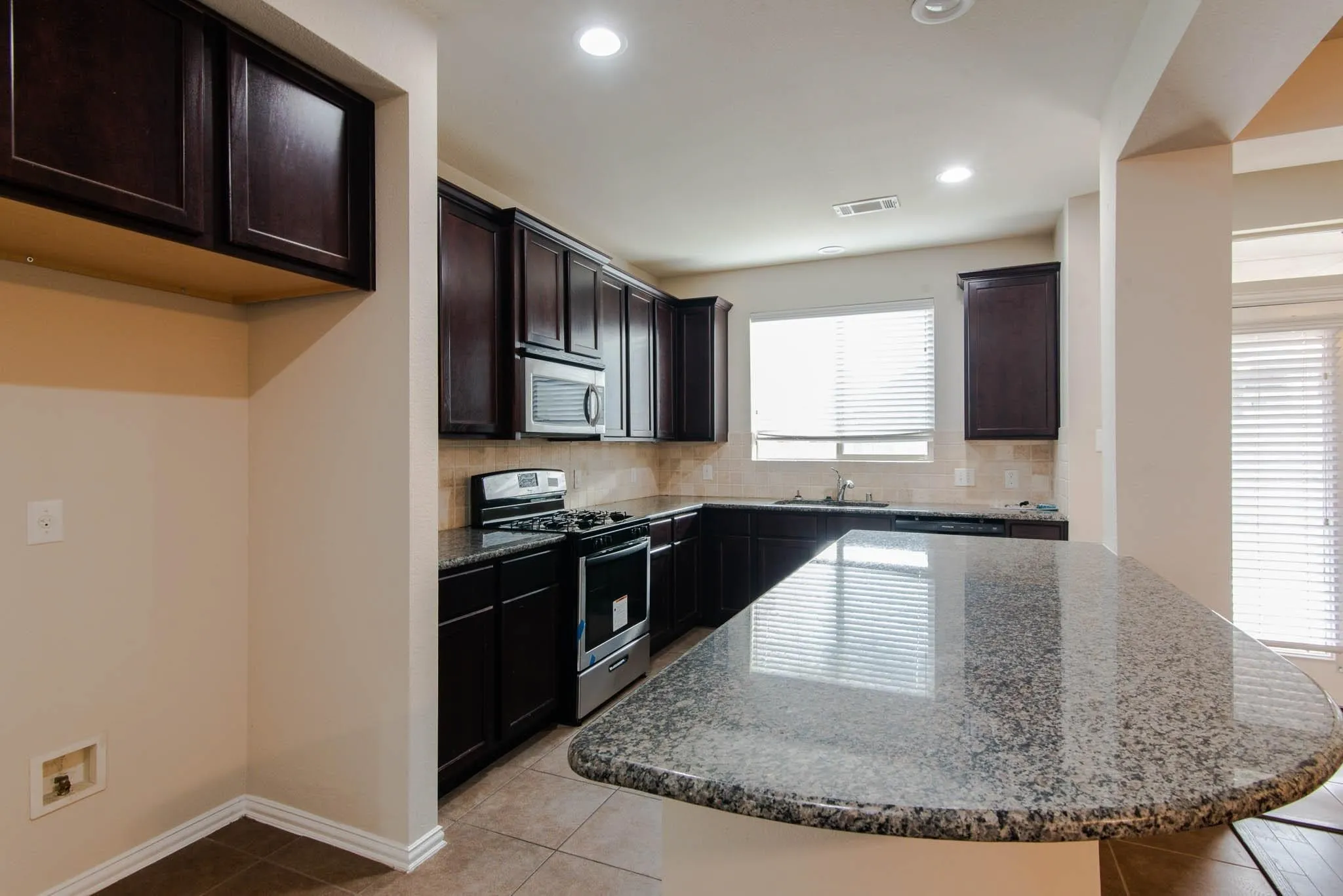 Kitchen featuring dark wood cabinetry, granite countertops, tile flooring, stainless steel appliances, and a built-in microwave
