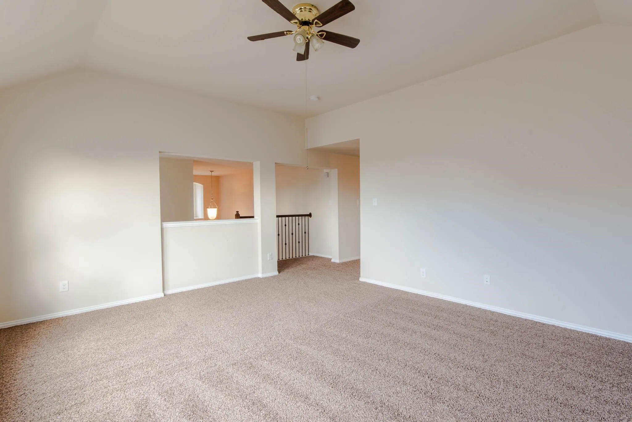 Vaulted ceiling living space featuring neutral tone carpeting and a brass-finish ceiling fan